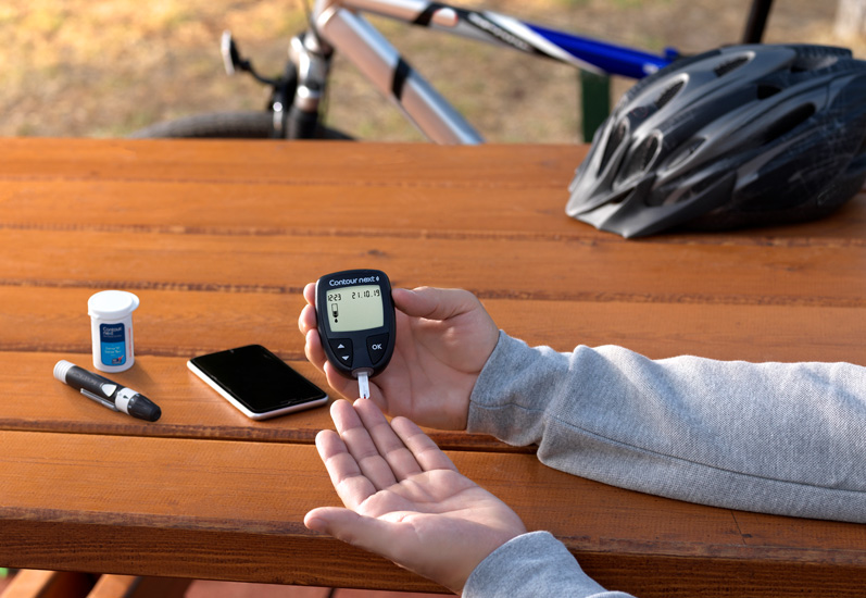 Hands holding a smartphone displaying glucose level chart reading "109 mg/dL" with time stamps in an outdoor setting.