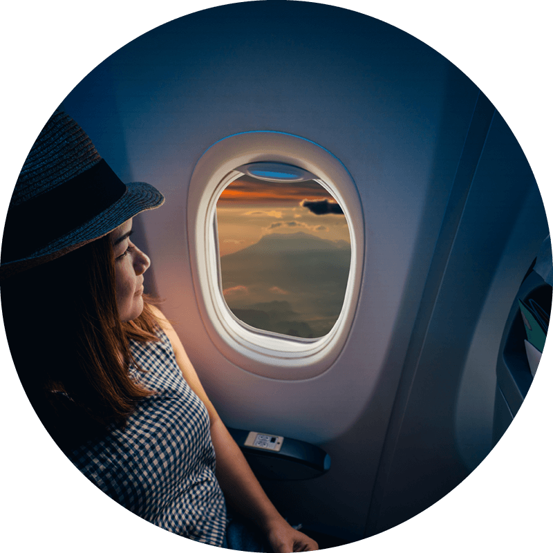 Eine Eversense Benutzerin reist mit einem CGM-Gerät, während sie einen Hut trägt und entspannt aus dem Flugzeugfenster blickt.