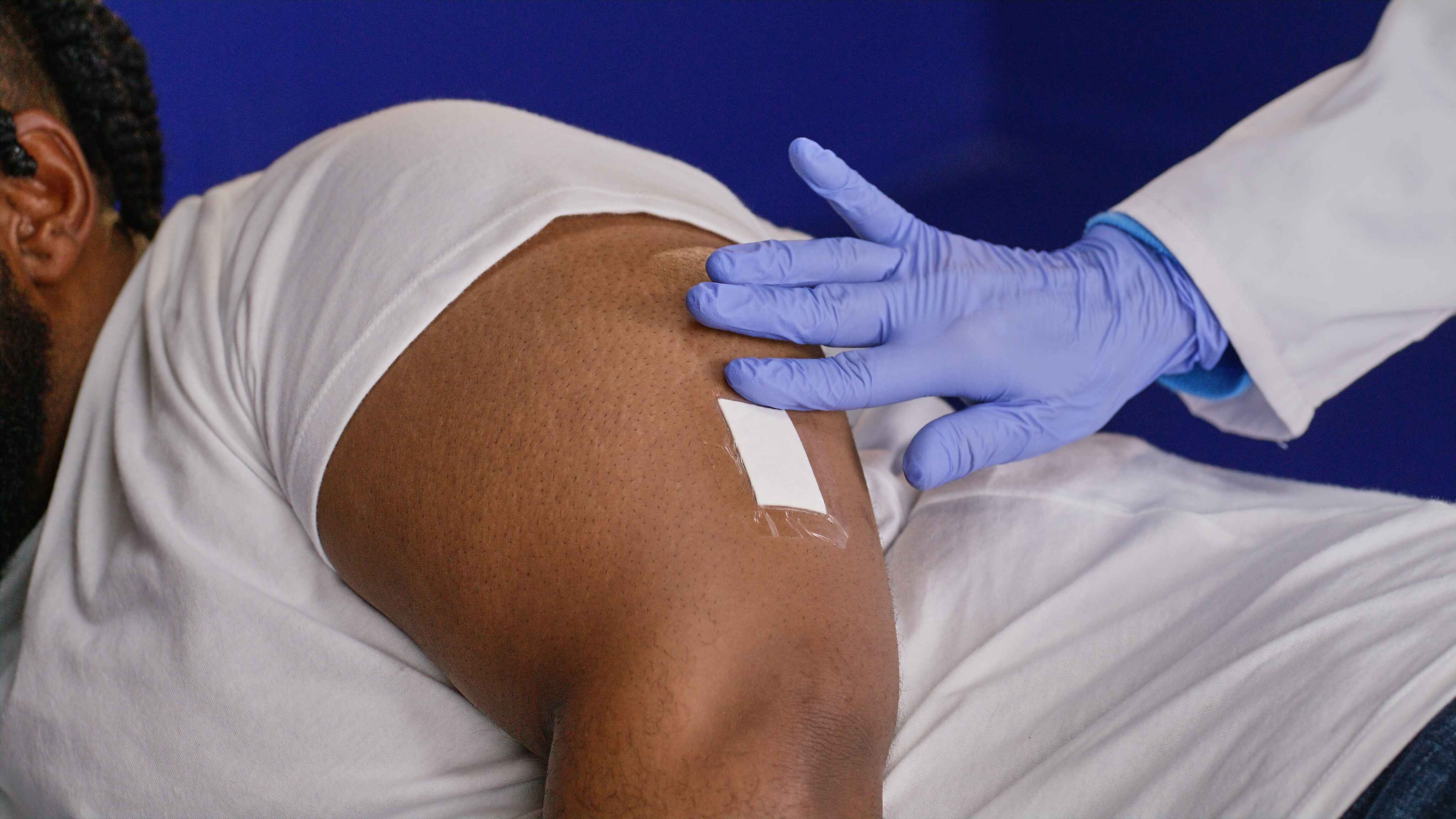 Gloved hand gently presses a small adhesive bandage onto the patient’s upper arm after completing the Eversense CGM sensor placement.